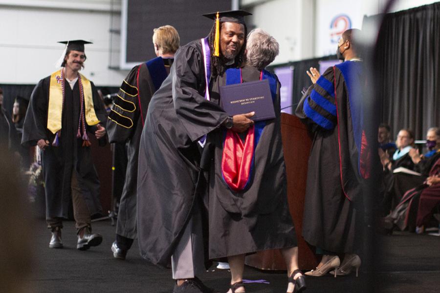 A student crosses the stage in cap and gown.