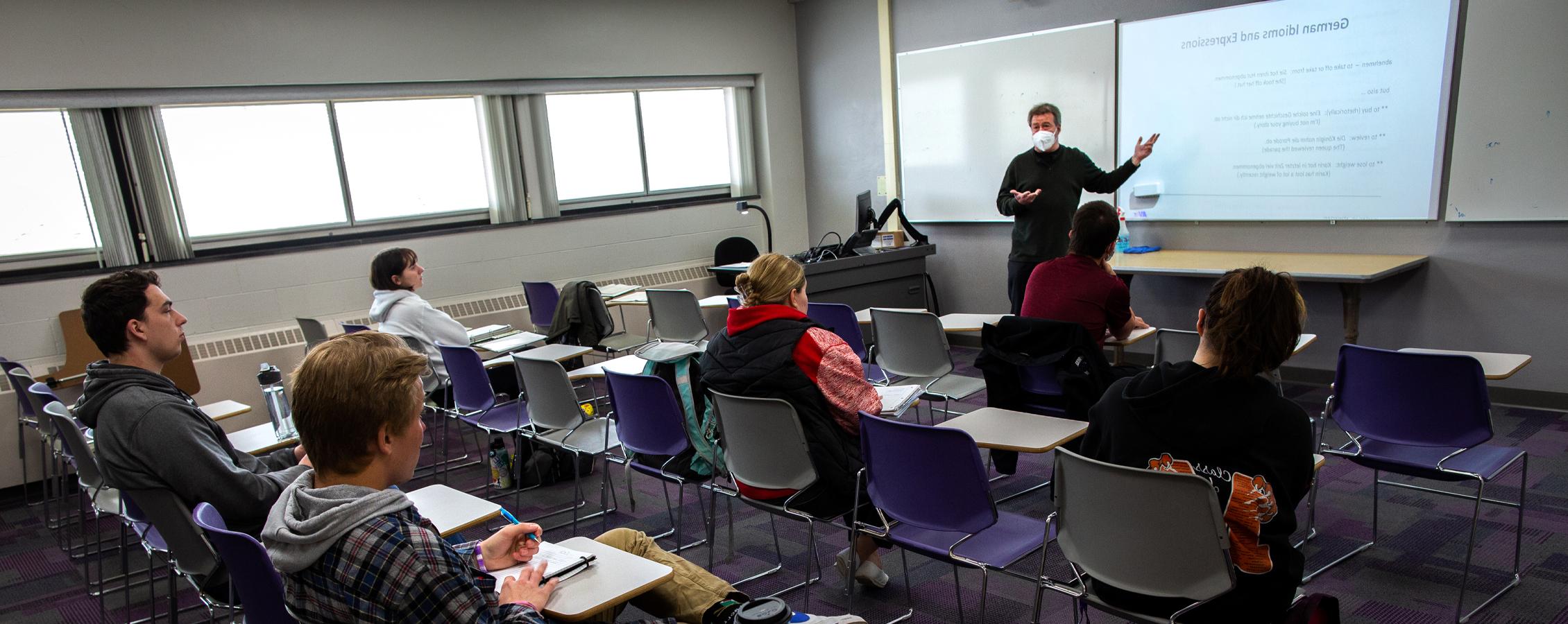 A German faculty member speaks by a whiteboard during class.