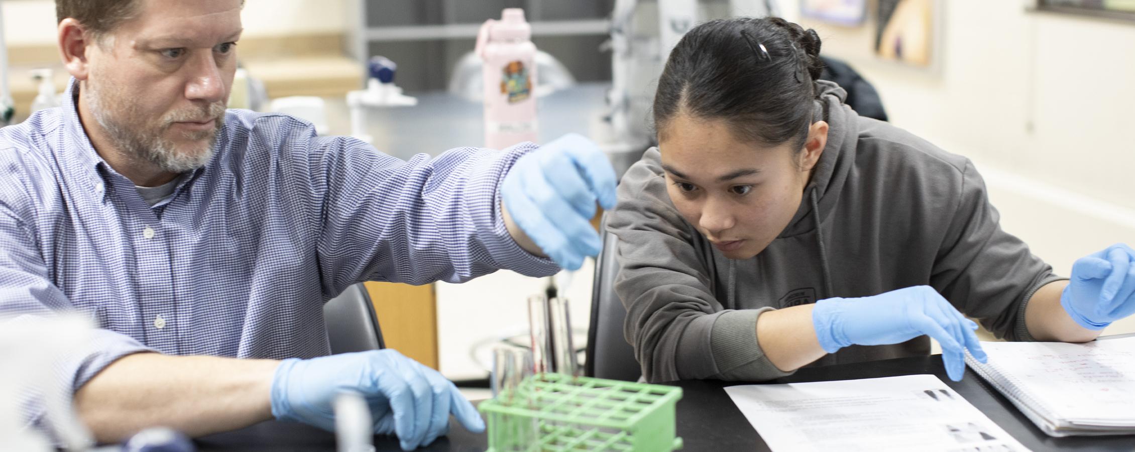 A student works in a lab with a faculty member.