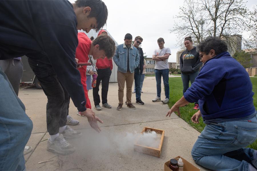 A faculty members demonstrates volcanic activity as smoke rises from a box.