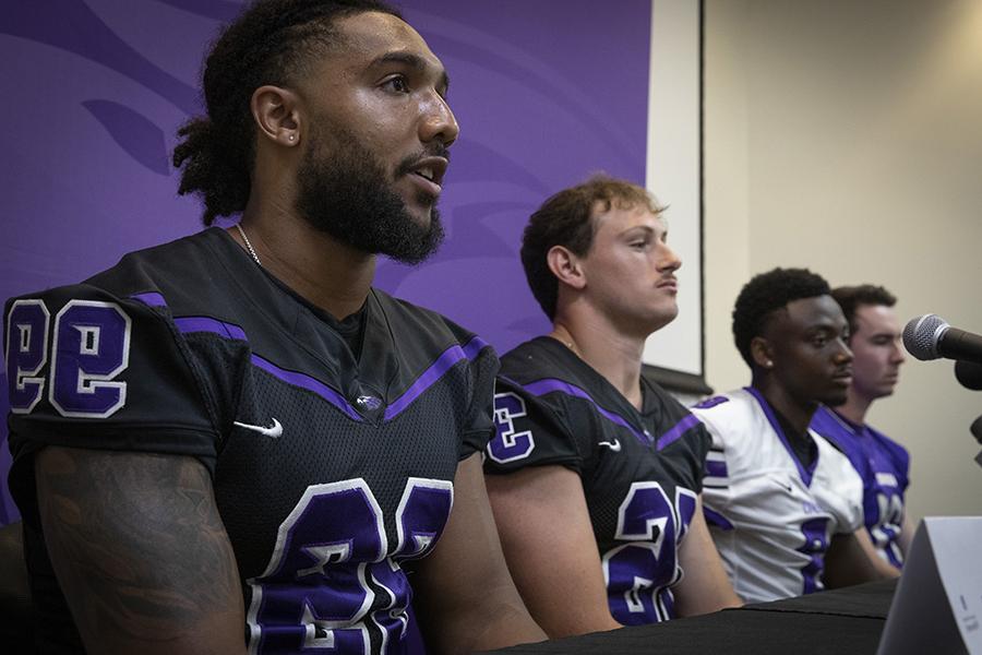 Warhawk football players wear their jerseys and sit together by a microphone during a press conference.