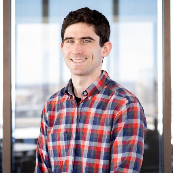 Photo of Caleb Flack sitting in front of a window wearing a red and blue plaid shirt