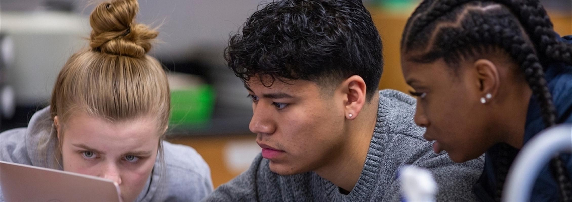 Three students work on a computer.