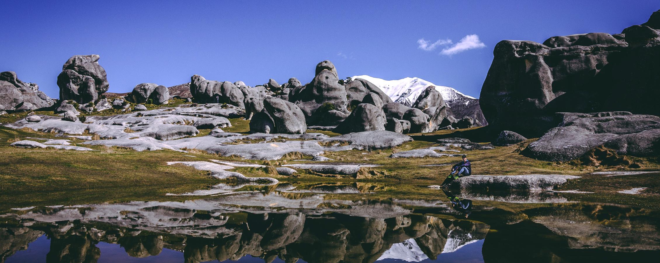 A person sits next to a pool of water amidst trees and mountains.