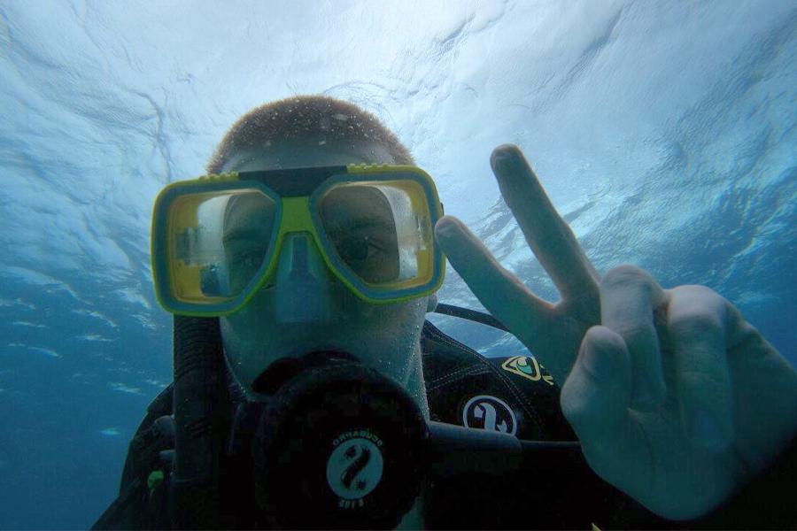 An underwater shot of a student wearing scuba gear makes a peace sign with his fingers.