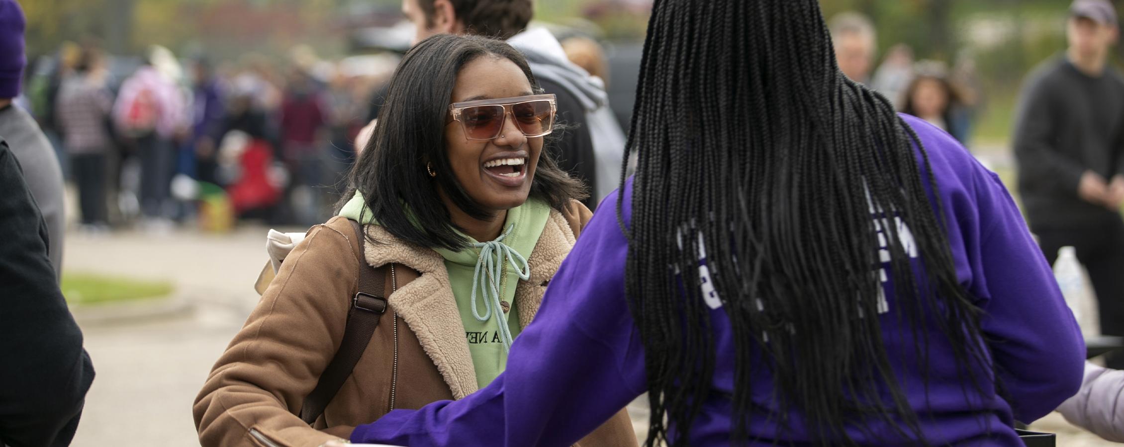 Two students smile and hug outside during a tailgate.