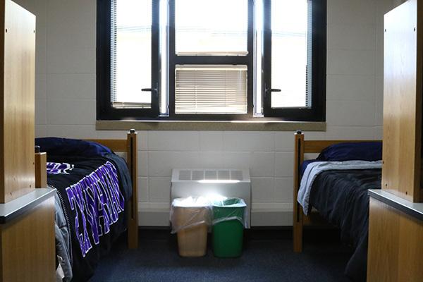 A dorm room with 2 beds and 2 desks, and 2 waste bins in it.