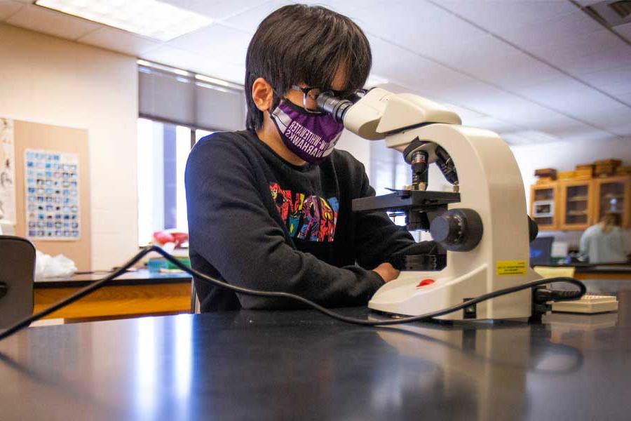 A student is working in the lab next to a microscope.