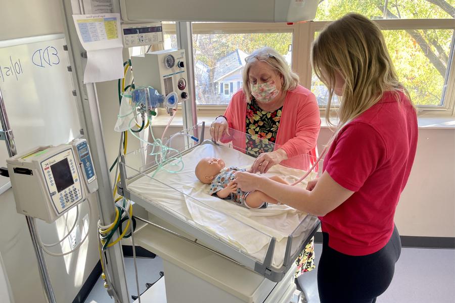 A student works a faculty member with a baby doll in a simulated hospital room.