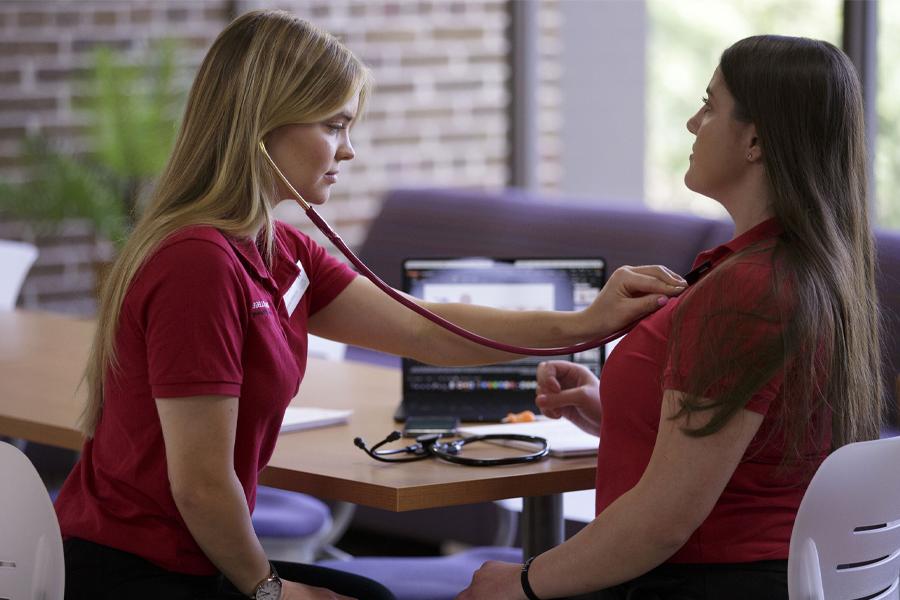 A student uses a stethoscope to listen to another student's chest.